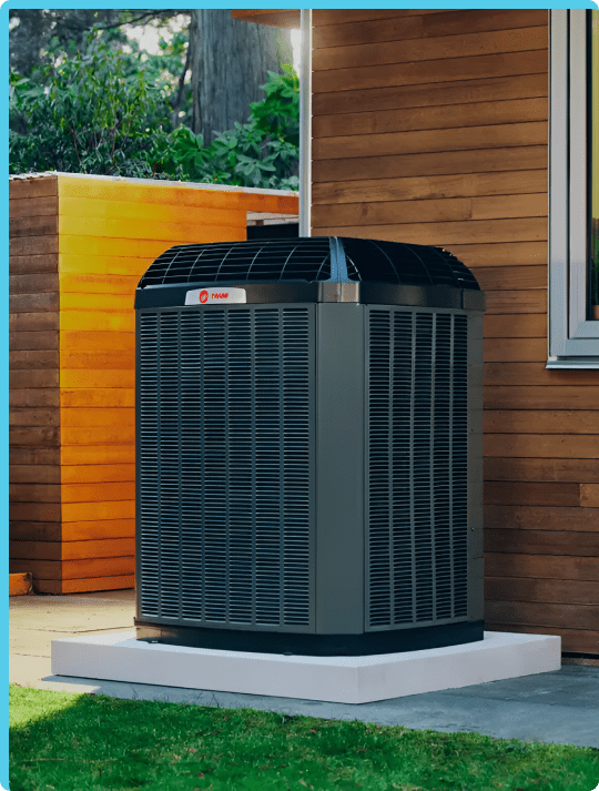 Outdoor air conditioning unit set on a concrete base near a wooden exterior wall
